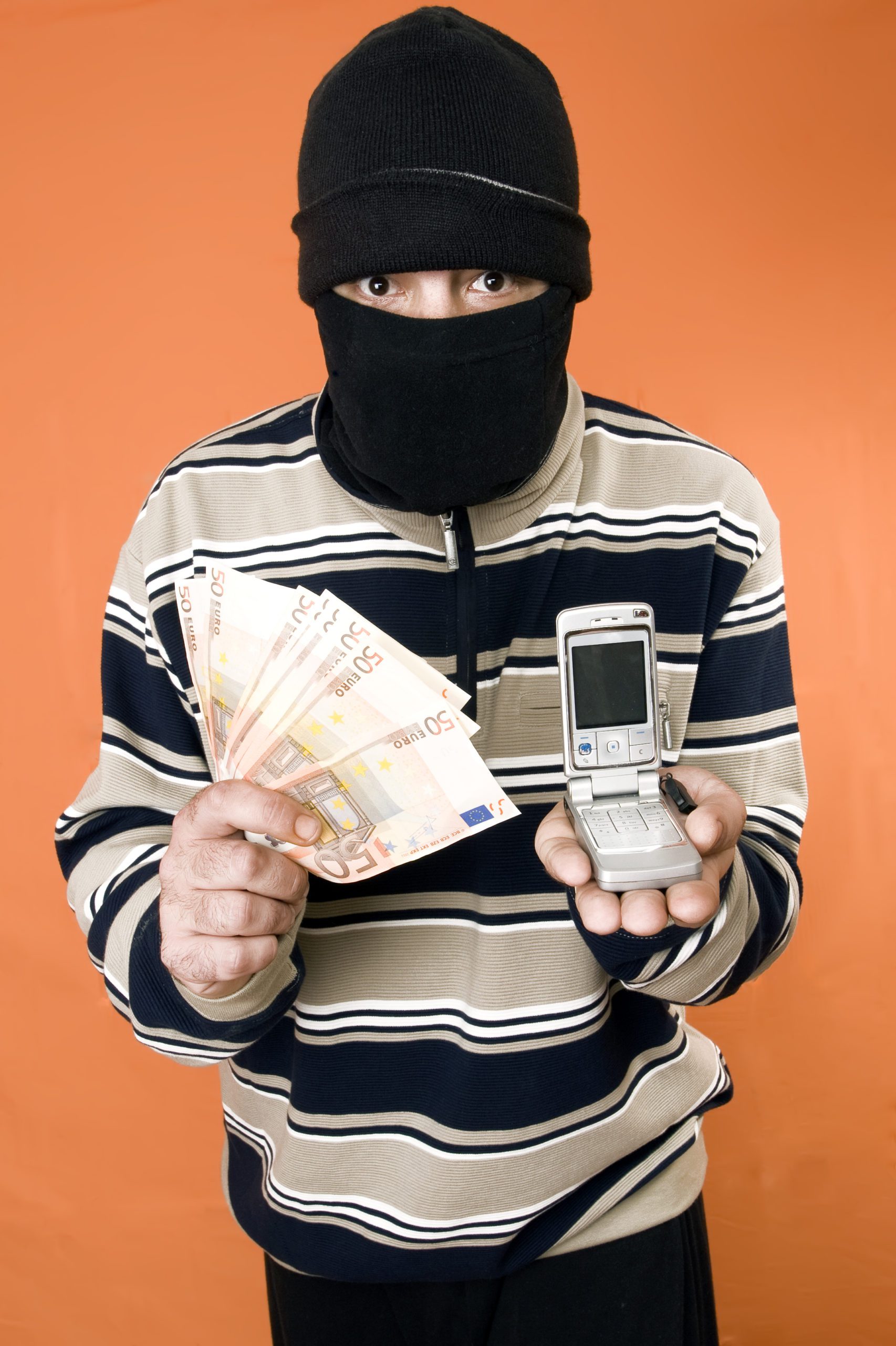 masked man with money in one hand and on the other hand a mobile phone