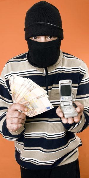 thief masked man with money in one hand and on the other hand a mobile phone